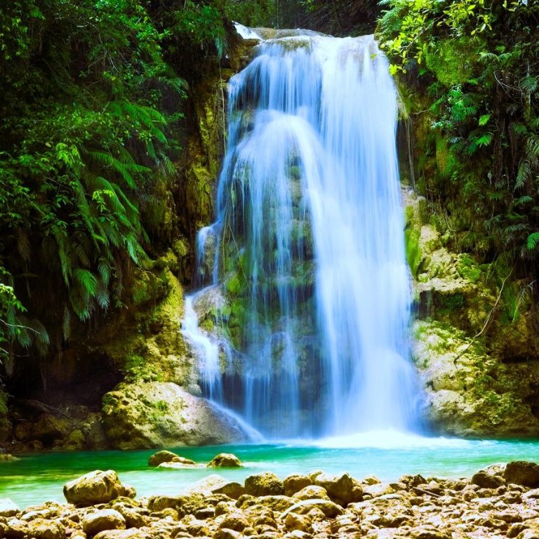 Ein Wasserfall fließt über grün bewachsene Felsen in ein klares, türkisfarbenes Becken.
