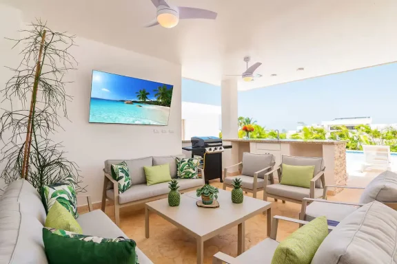 Moderne Außenlounge mit bequemen Möbeln und TV, Blick auf einen Pool und eine tropische Landschaft.