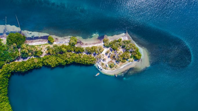 Luftaufnahme einer tropischen Insel mit klarem Wasser und üppiger Vegetation.